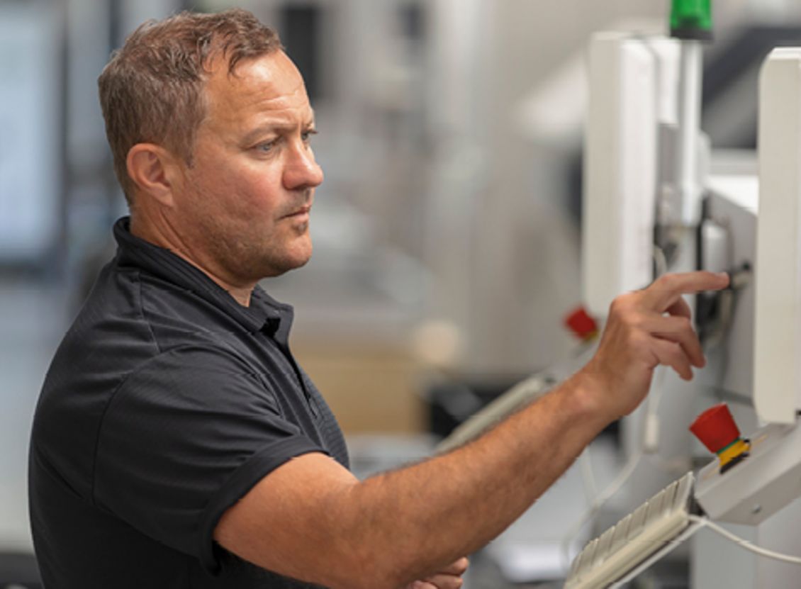 Ein Mitarbeiter der FSM AG bedient eine Produktionsmaschine in der Produktionsumgebung des Unternehmens, mit Fokus auf die Steuerungselemente der Anlage.